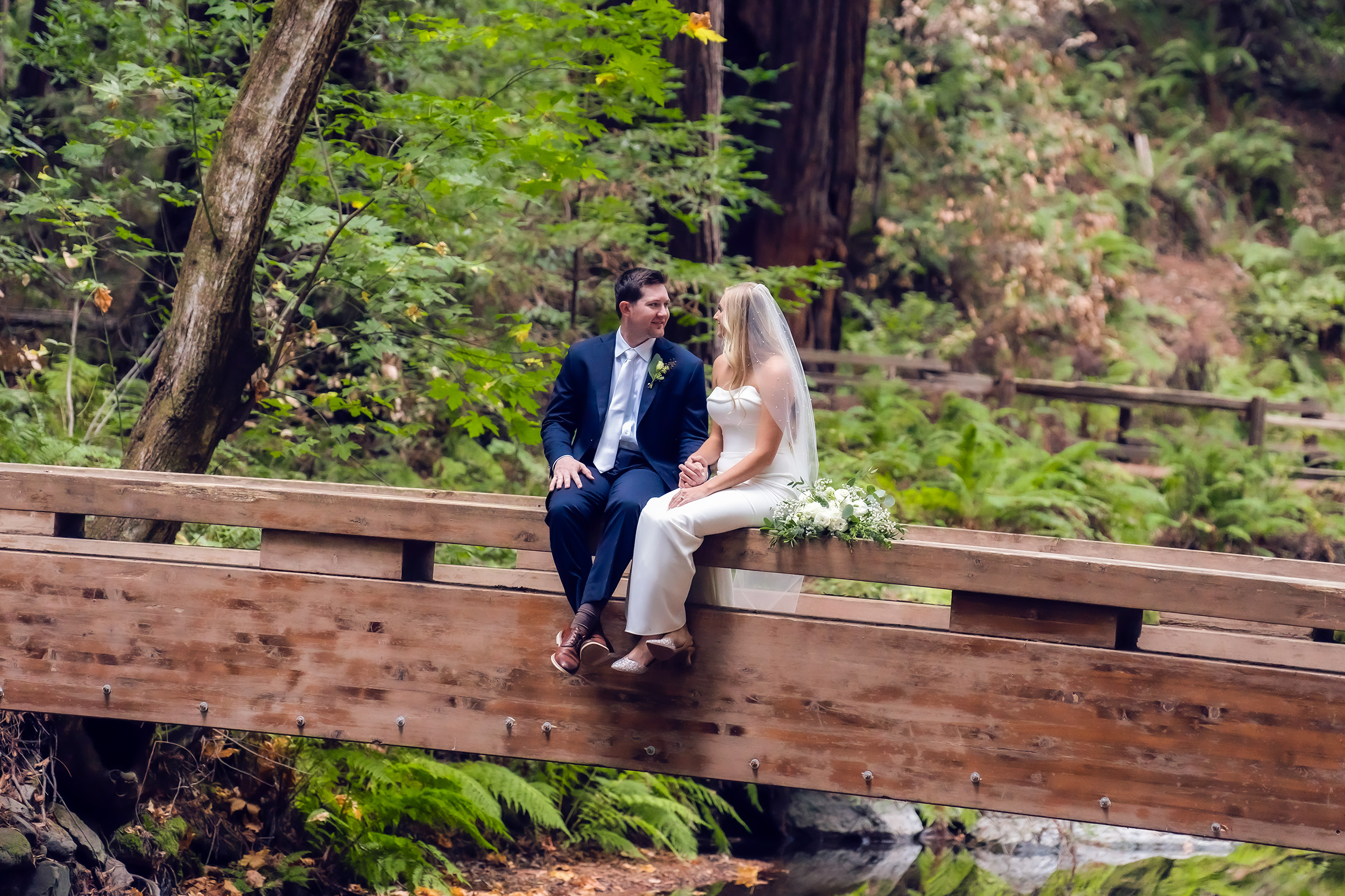 Photography of an eloping couple in Muir Woods holding hands sitting on a natural bridge